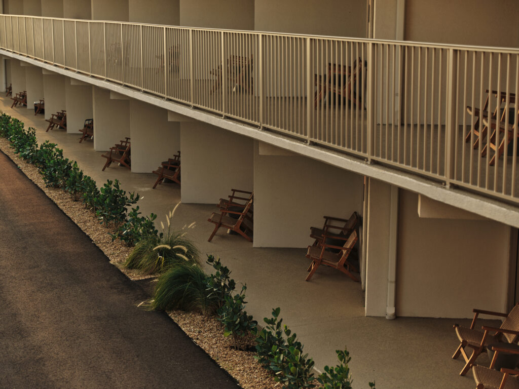 Row of private patios at Ambros Hotel with woven lounge chairs, coastal landscaping, and soft evening light.