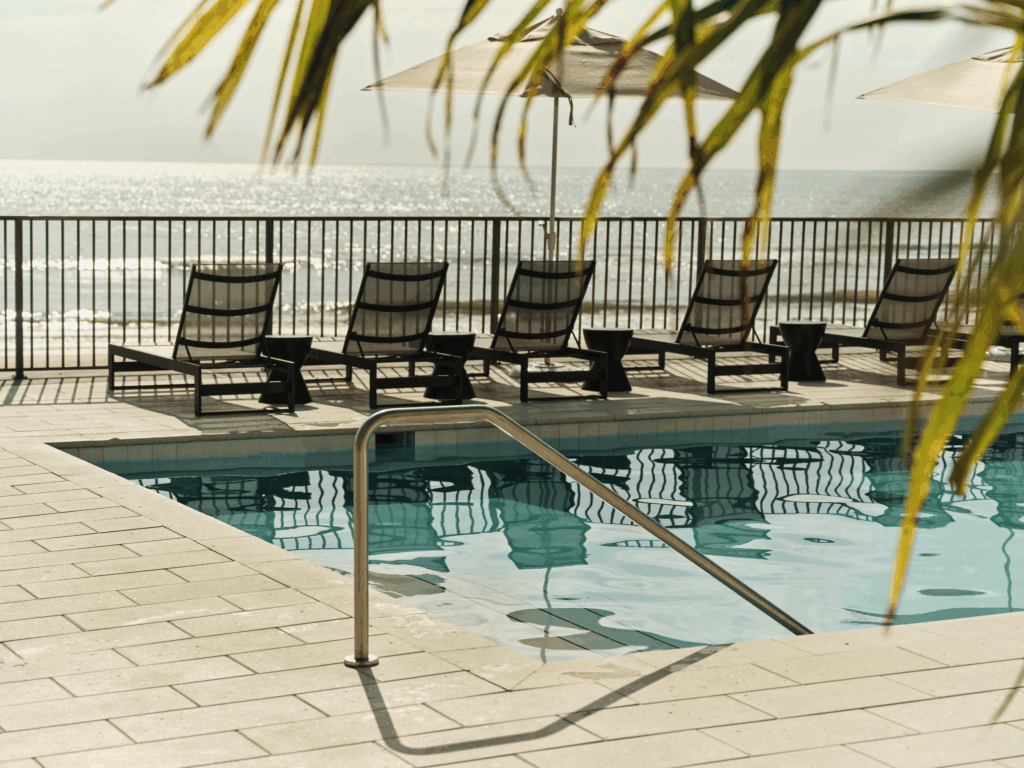 Oceanfront pool at Ambros Daytona Beach with lounge chairs and umbrellas under the sun.