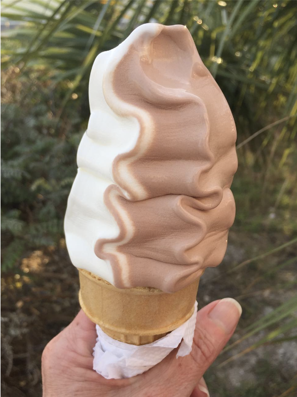 Close-up of a hand holding a vanilla and chocolate swirl soft-serve ice cream cone from the Dairy Bar.