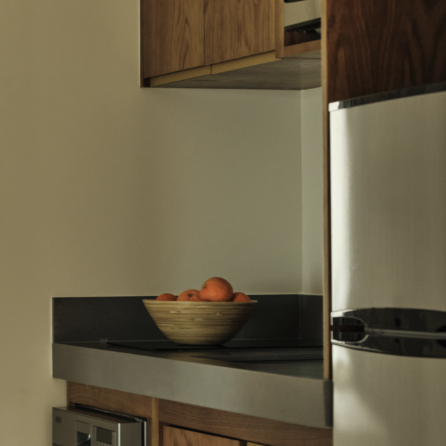 Kitchenette in the Executive King Suite at Ambros Hotel with wood cabinetry, stainless steel appliances, and a bowl of fresh oranges