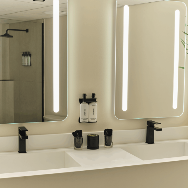 Modern double vanity bathroom at Ambros Hotel with backlit mirrors, matte black fixtures, and luxury amenities