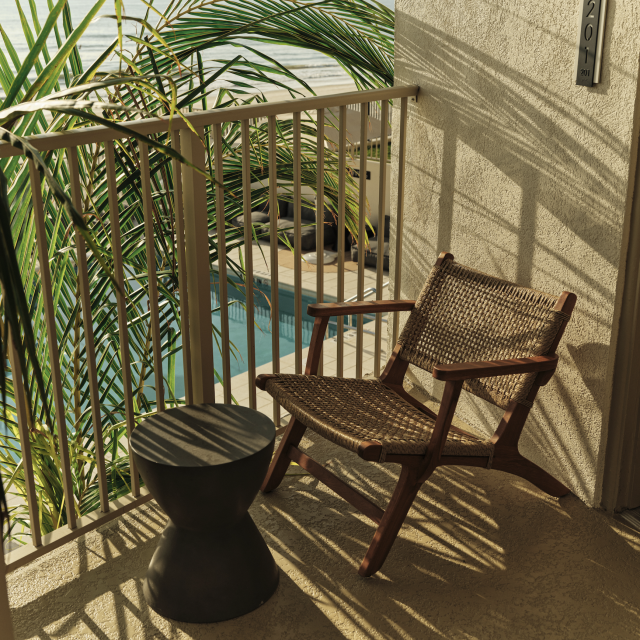 Private balcony of the Oceanfront King Suite at Ambros Hotel with rattan chair, tropical plants, and ocean breeze