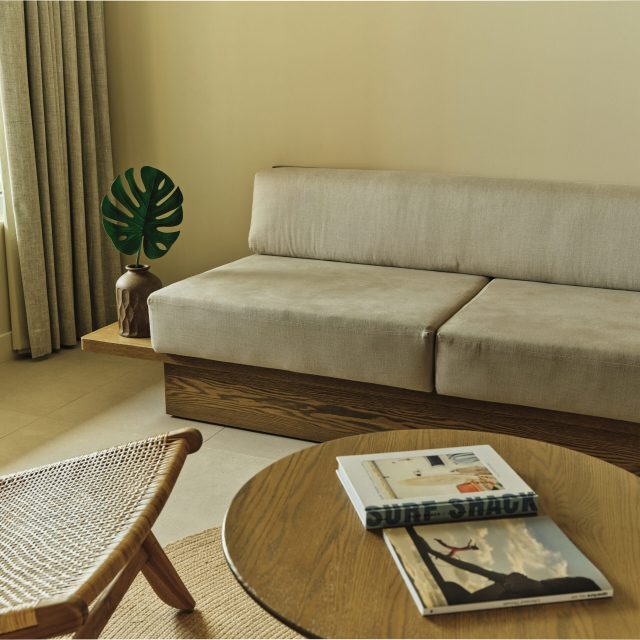 Lounge area in the Ambros King Suite with neutral sofa, rattan chair, coffee table, and tropical decor