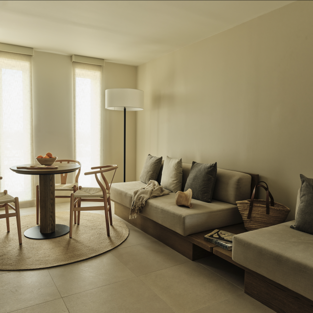 Living room in the One Bedroom Suite at Ambros Hotel featuring built-in sofa seating, round dining table, and soft neutral décor
